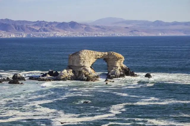 Arco de roca de La Portada en el mar, con la costa de Antofagasta y cerros al fondo