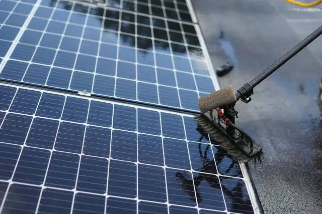 Cepillo suave con pértiga limpiando con agua la superficie de unos paneles solares